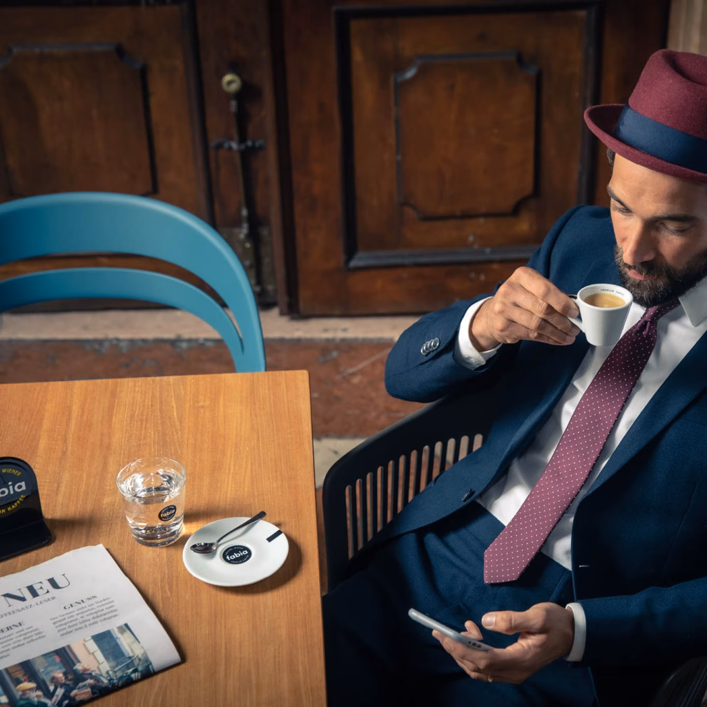 Imagebild junger Mann im Anzug mit Hut und Krawatte mit einer Tasse fabia Wiener Premium Kaffee in der Hand